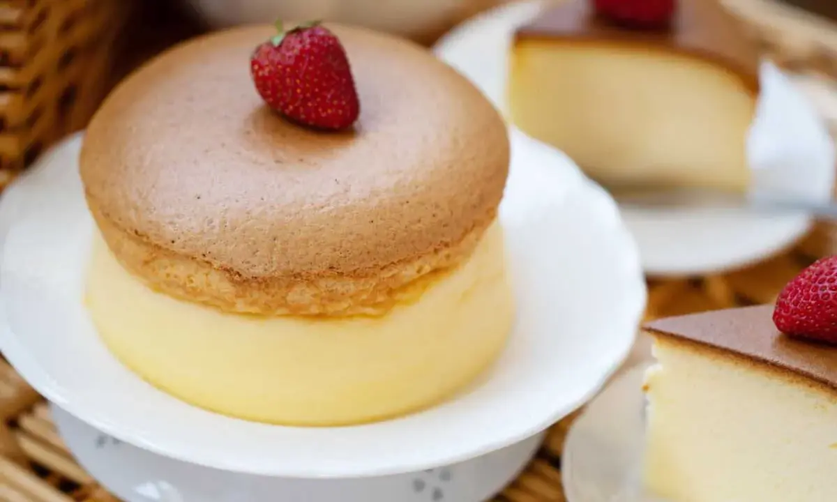 Un délicieux cheesecake japonais aérien, garni d'une fraise fraîche. Une tranche de ce dessert léger et moelleux est servie sur une assiette.