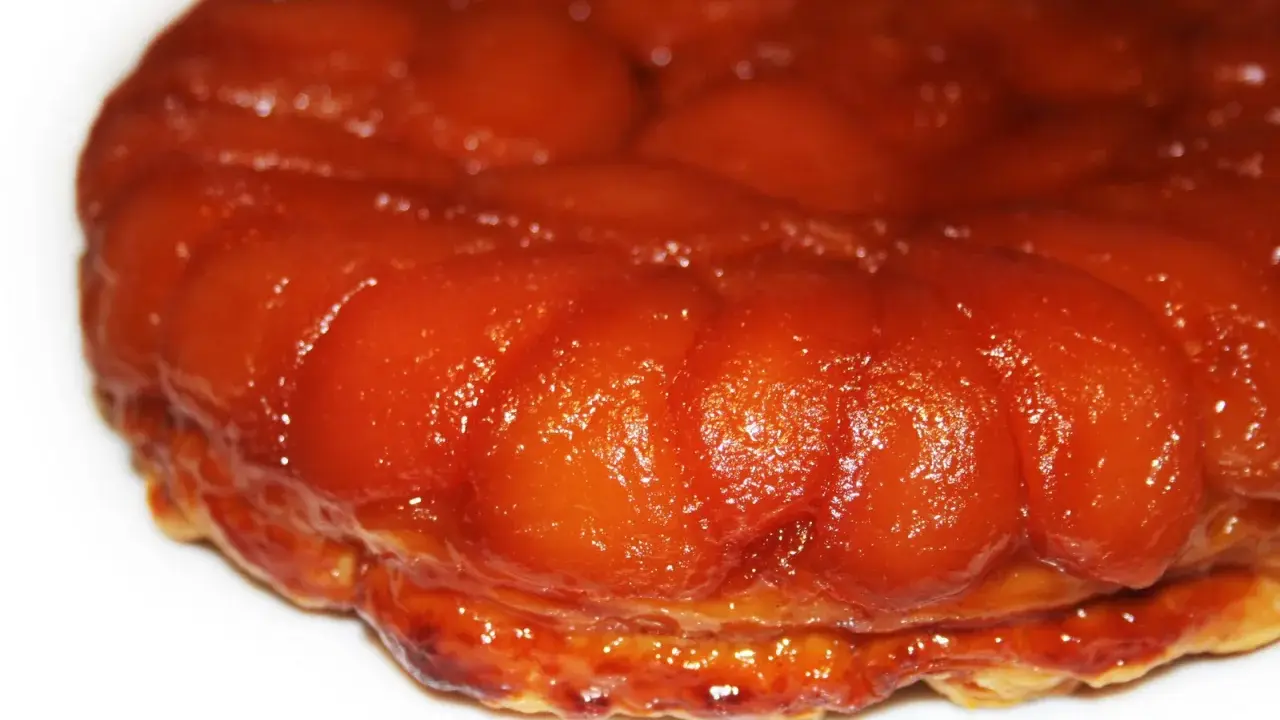 Gros plan sur une délicieuse tarte tatin aux pommes caramélisées, sa pâte dorée et ses fruits brillants invitent à la dégustation.