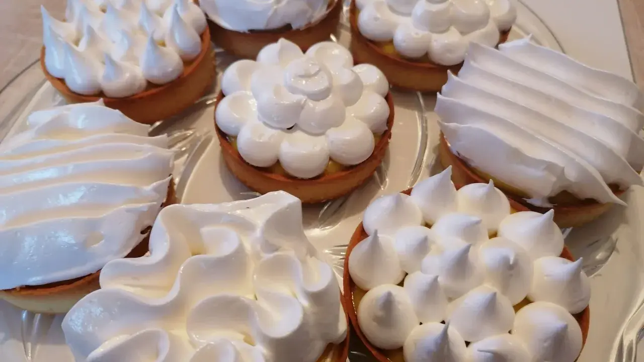Assortiment de tartelettes garnies d'une crème citron et surmontées de **meringue italienne** aux formes variées.