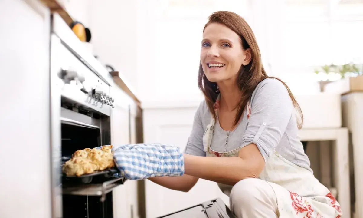 Femme souriante sortant un plat du four. Une recette de pain à la chaleur tournante humide parfaite.