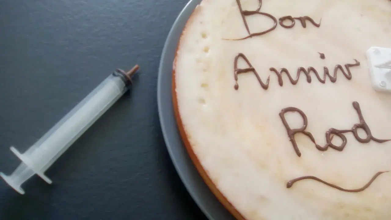 Glaçage pour écrire sur un gâteau : "Bon Anniv Rod". Une seringue est à côté, prête pour la décoration.