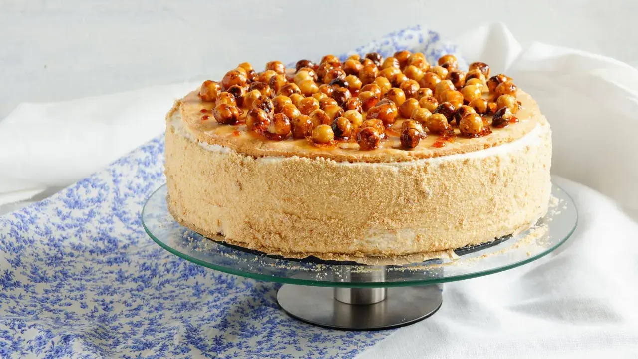 Gâteau dacquoise noisette garni de noisettes caramélisées sur un présentoir en verre.