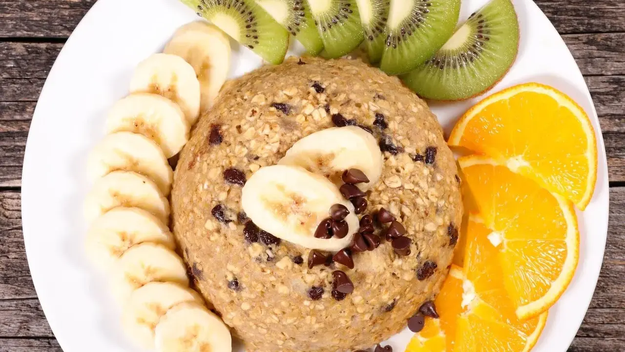 Un délicieux bowl cake flocon d'avoine garni de rondelles de banane, de tranches de kiwi et d'orange, parsemé de pépites de chocolat.