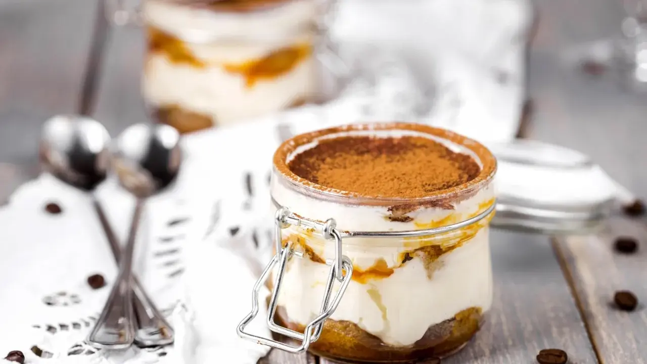 Deux bocaux de tiramisu, le meilleur dessert, saupoudrés de cacao, avec des grains de café et des cuillères sur une nappe en dentelle.