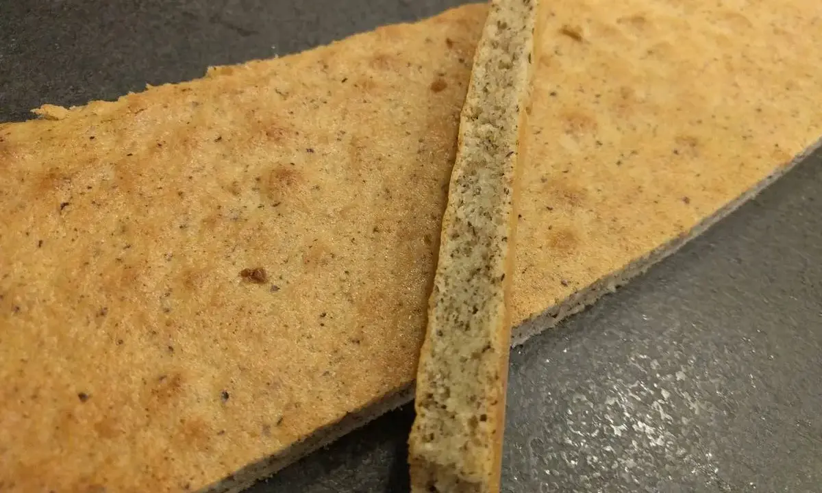 Deux fines tranches de biscuit moelleux noisette, parsemées de petits grains, reposent sur une surface sombre.