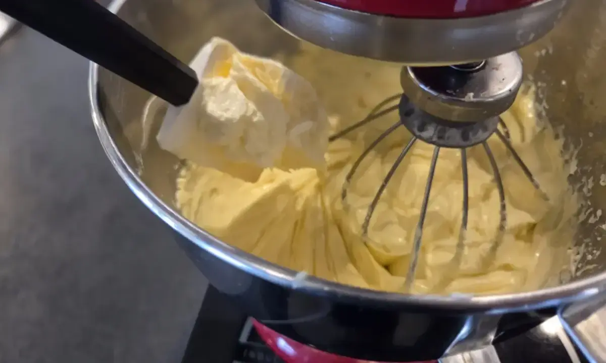 Préparation d'une crème mousseline chantilly onctueuse dans un robot pâtissier. Une spatule ajoute une touche de douceur.