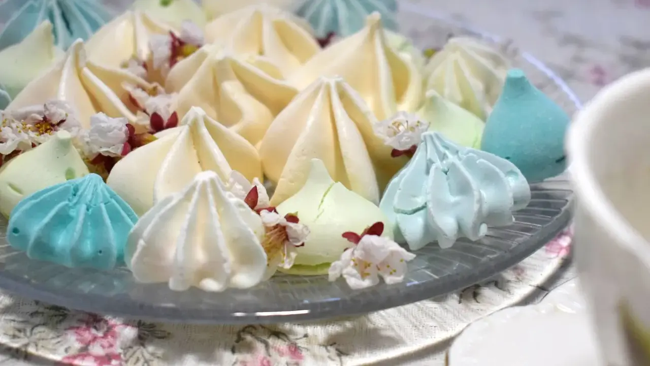 Meringues colorées, comme créées par un robot pâtissier, parsemées de fleurs délicates.