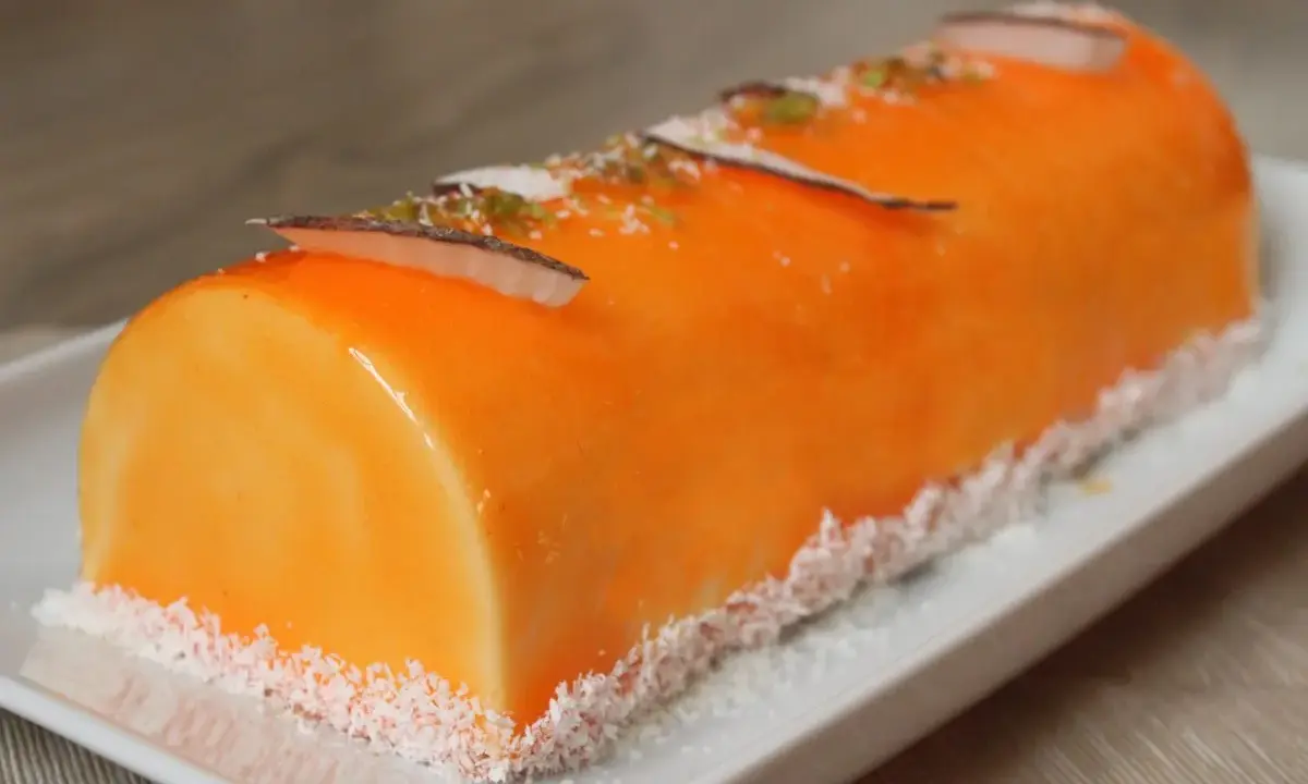 Bûche fruit exotique, un délice orangé glacé, décoré de copeaux de noix de coco et de zestes verts.