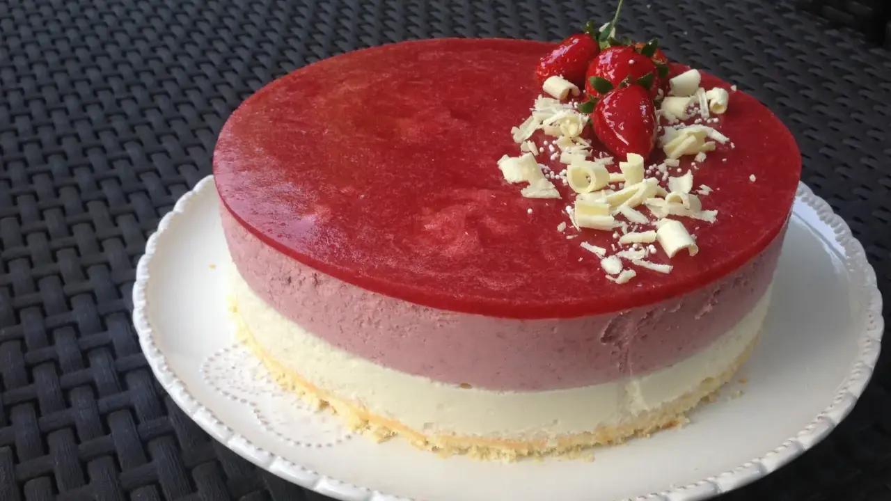 Un délicieux entremet aux trois couches, couronné d'une mousse fraise, de fraises fraîches et de copeaux de chocolat blanc. Parfait pour une occasion spéciale.