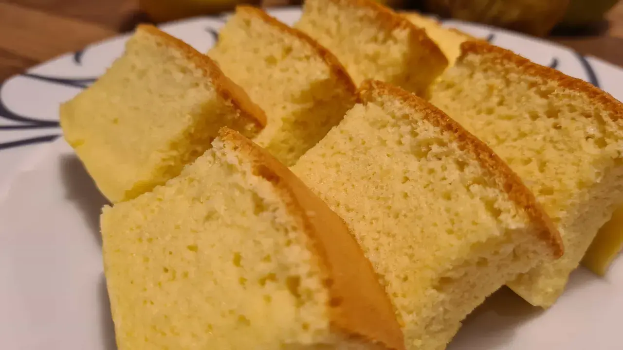 Tranches de moelleux gâteau japonais, léger et aérien, sur une assiette blanche. Des fruits jaunes sont flous en arrière-plan.