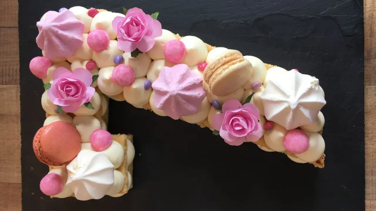 Un biscuit joconde number cake en forme de 1, décoré de crème, meringues, macarons et roses en sucre.
