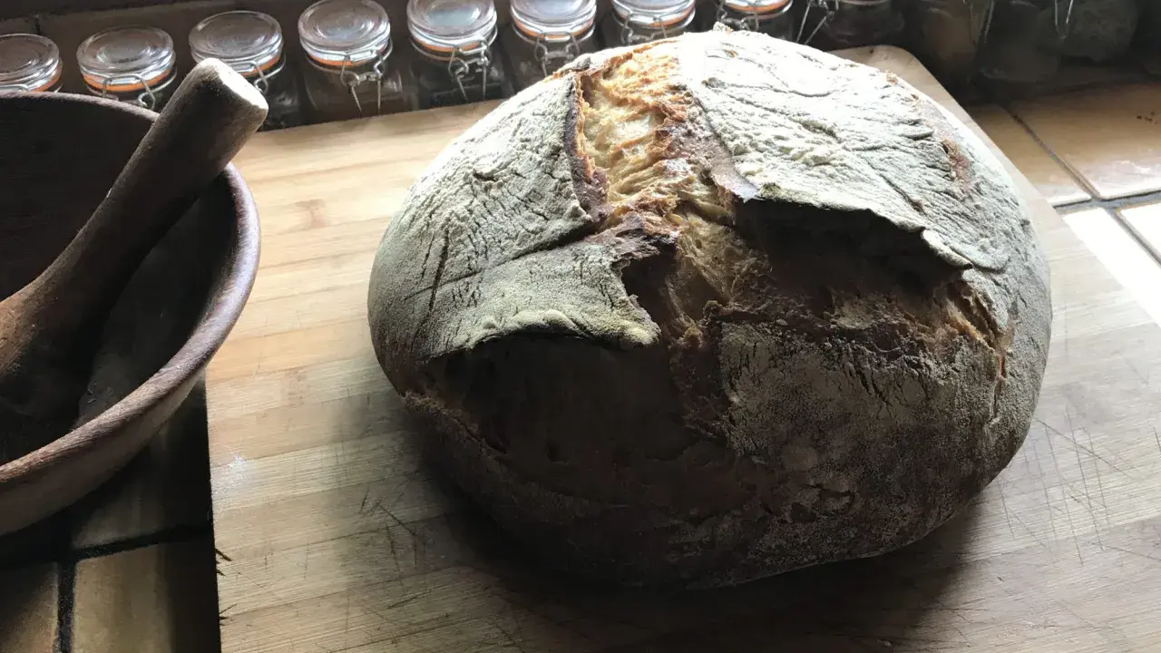 Gros pain artisanal sur une planche en bois, avec un mortier à côté. La question "peut on mélanger levain et levure" plane dans l'air.