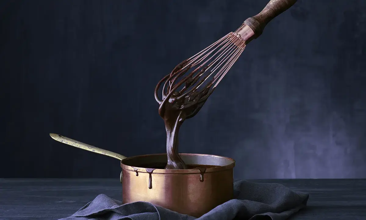 Sauce chocolat qui ne fige pas, coulante et brillante, dégouline d'un fouet dans une casserole en cuivre.