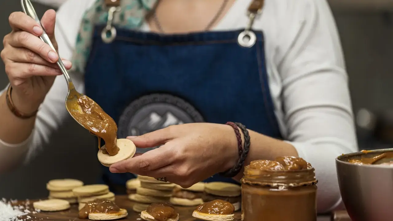 Une main dépose une cuillère de dulce de leche sur un biscuit rond, préparant des **caras crakine fait maison**.