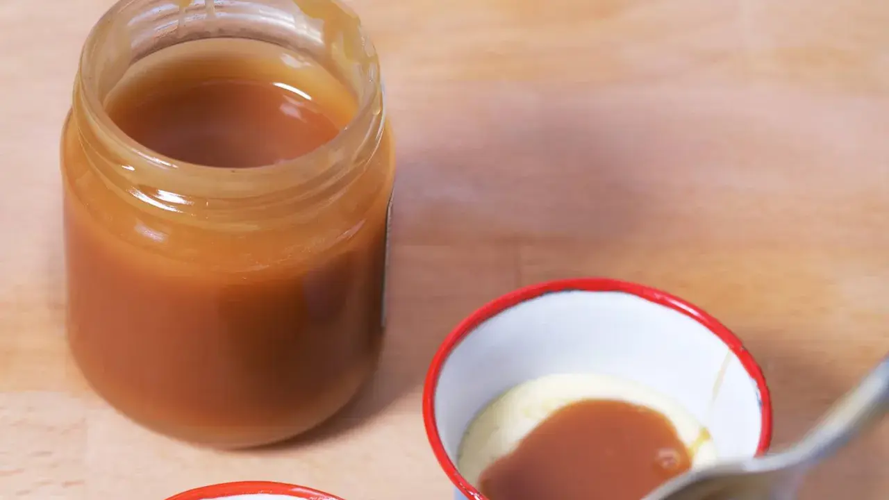 Un pot de caramel beurre salé sans beurre demi sel, prêt à être dégusté. Une cuillère est sur le point de plonger dans une petite coupelle de crème et de caramel.