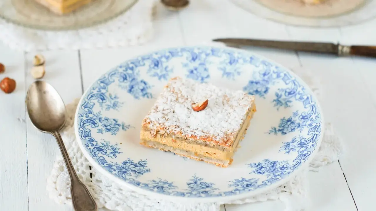 Un carré de gâteau russe, saupoudré de sucre glace et garni d'une noisette, sur une assiette ornée de bleu.