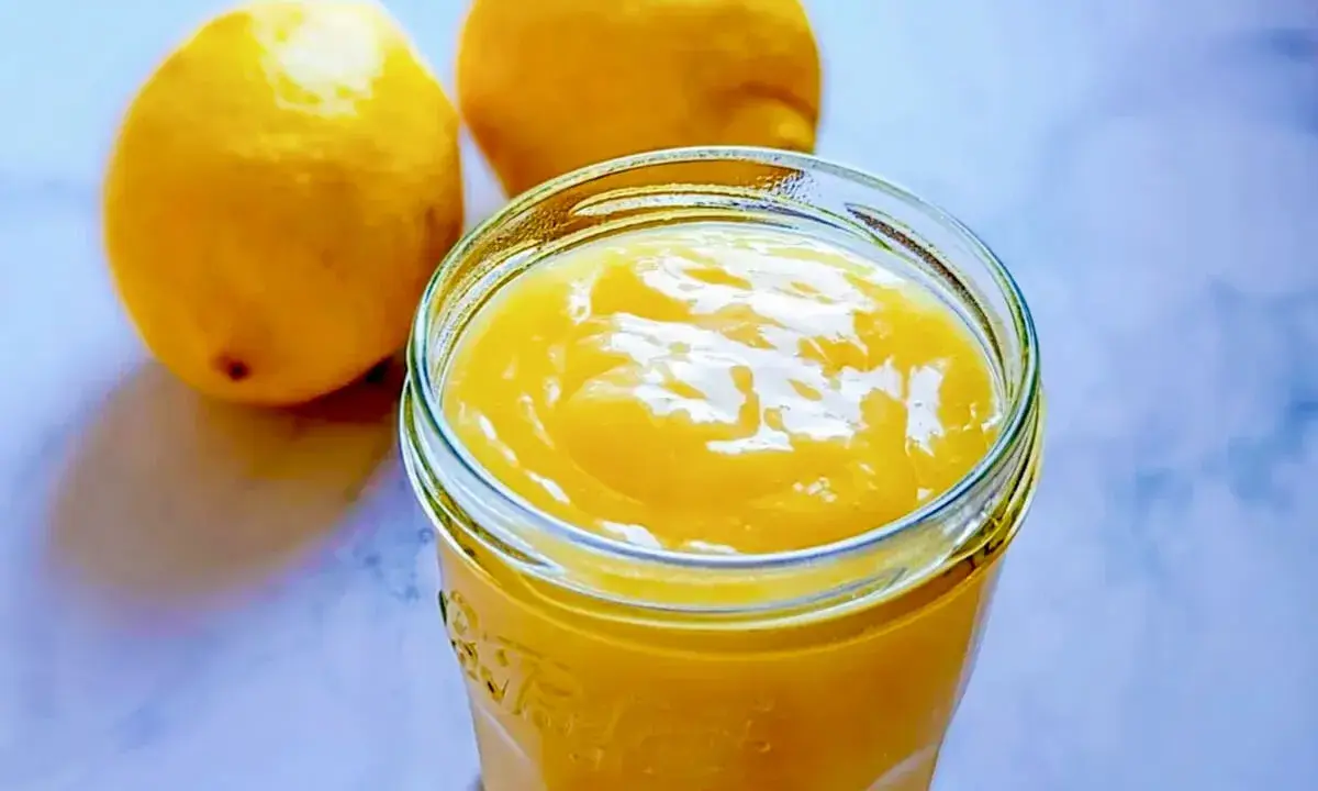 Un pot de crème citron onctueuse, parfaite pour une recette facile. Deux citrons frais à côté.