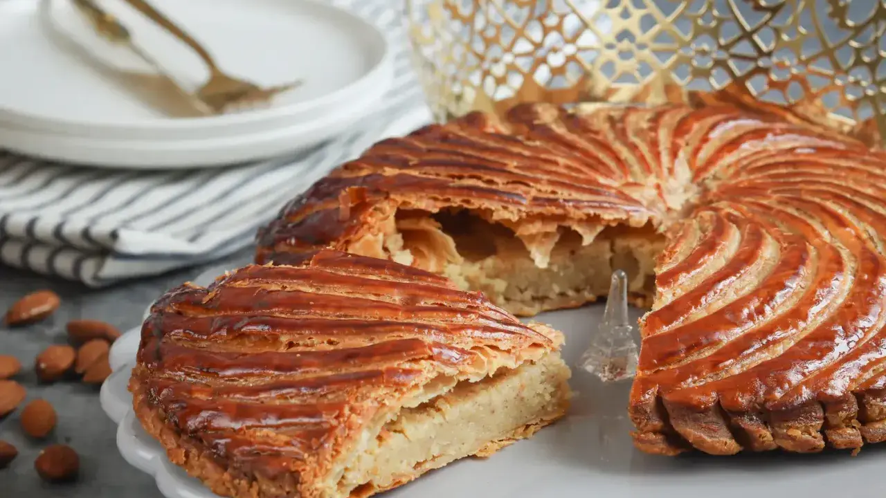 Galette des Rois dorée, garnie d'une généreuse crème d'amande. Une part est coupée, révélant sa texture feuilletée.