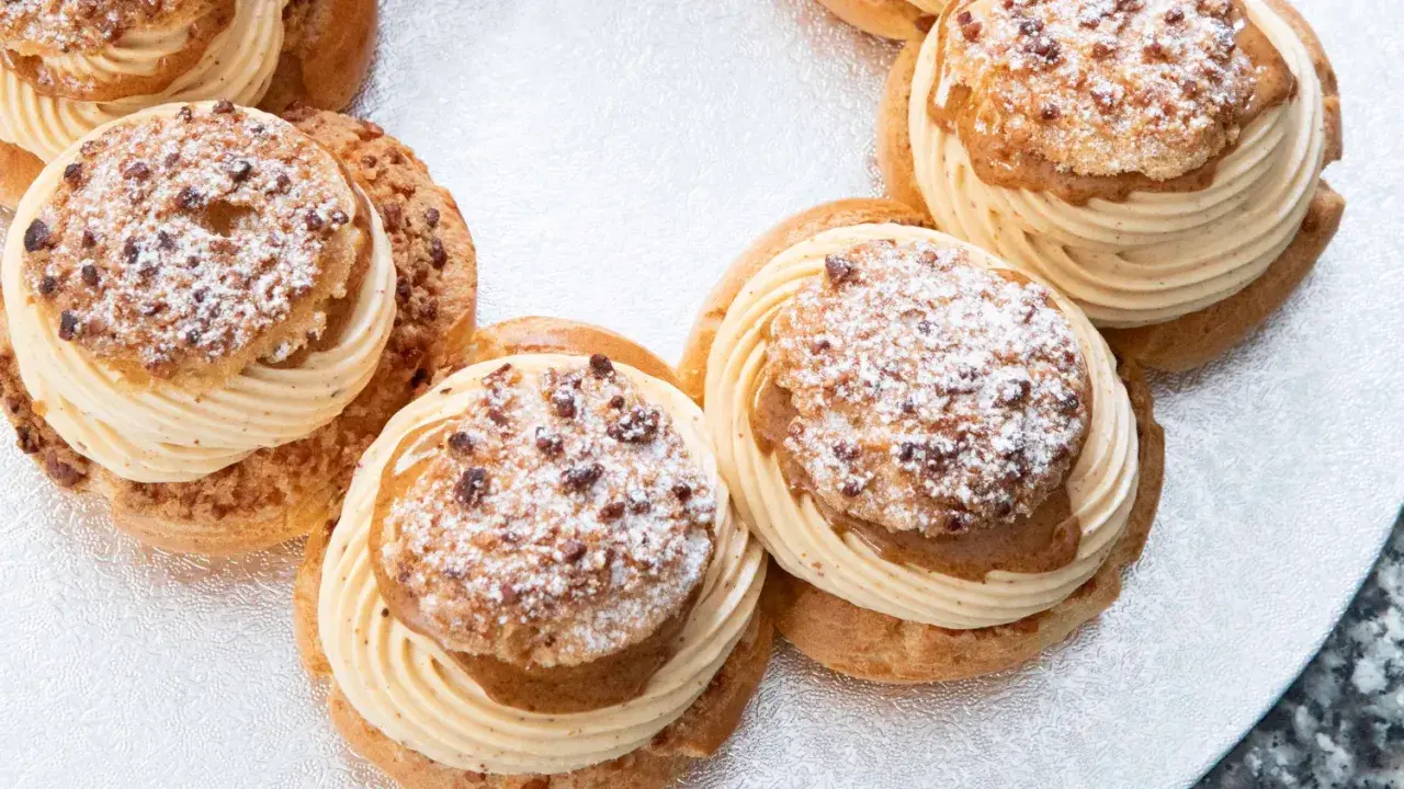 Plusieurs Paris-Brest, des pâtisseries rondes à la pâte à choux garnies de crème onctueuse et saupoudrées de sucre glace et d'amandes.