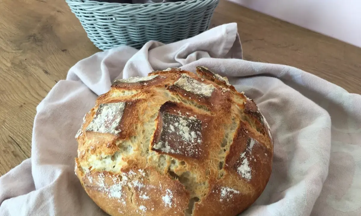 Un pain artisanal doré, prêt à être dégusté après son temps de pousse. Une corbeille de serviettes grises est visible en arrière-plan.