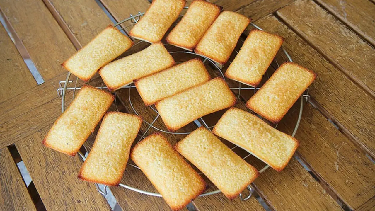 Douze biscuits financiers dorés, disposés sur une grille de refroidissement, sur une table en bois.