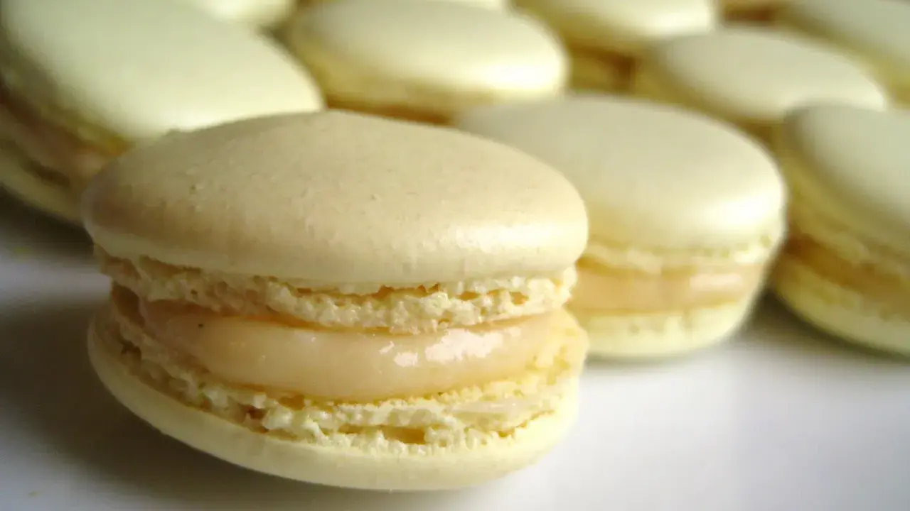 Un macaron meringue italienne, délicatement garni, se tient au premier plan, entouré d'autres douceurs pâles.
