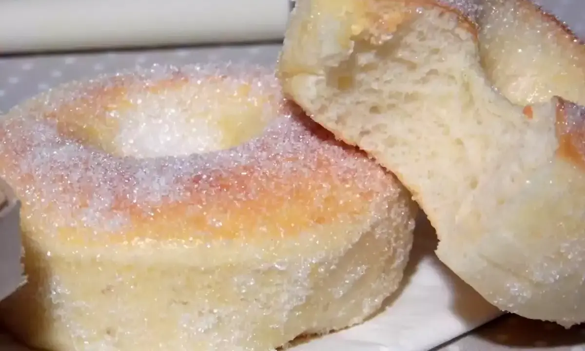 Deux beignets au four, saupoudrés de sucre, dont l'un est coupé, révélant une mie moelleuse.