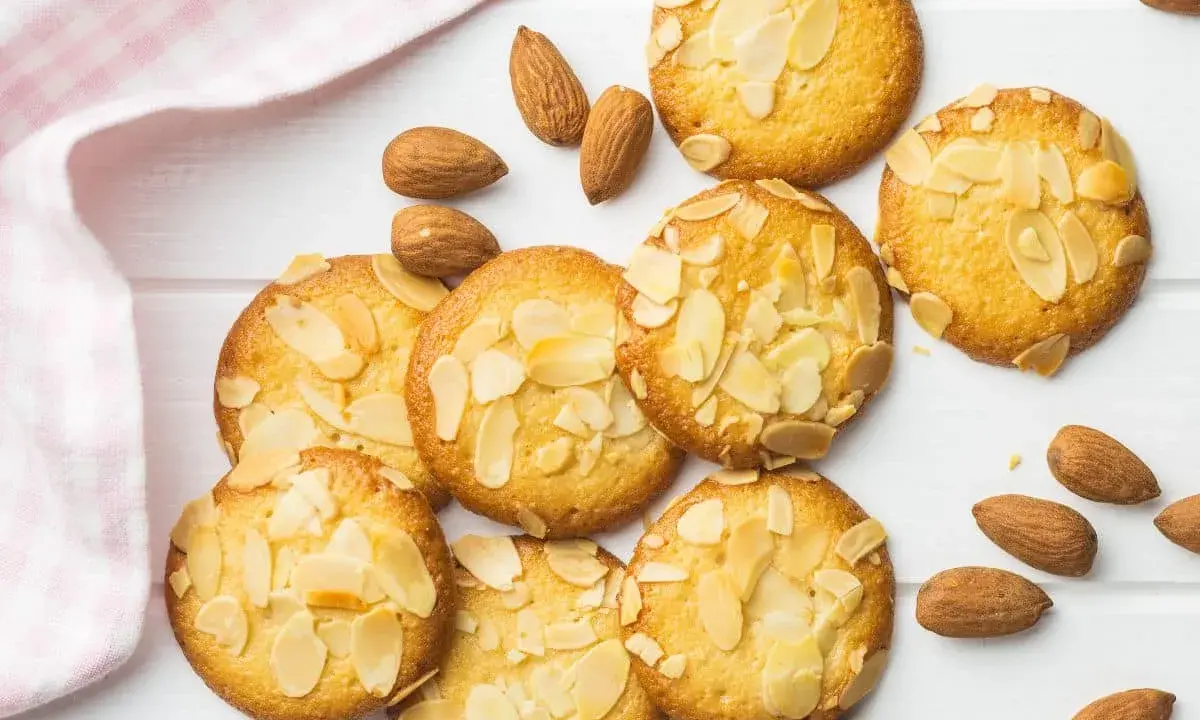 Des biscuits moelleux aux amandes, parsemés d'éclats d'amandes, sur un fond blanc avec une serviette à carreaux roses.