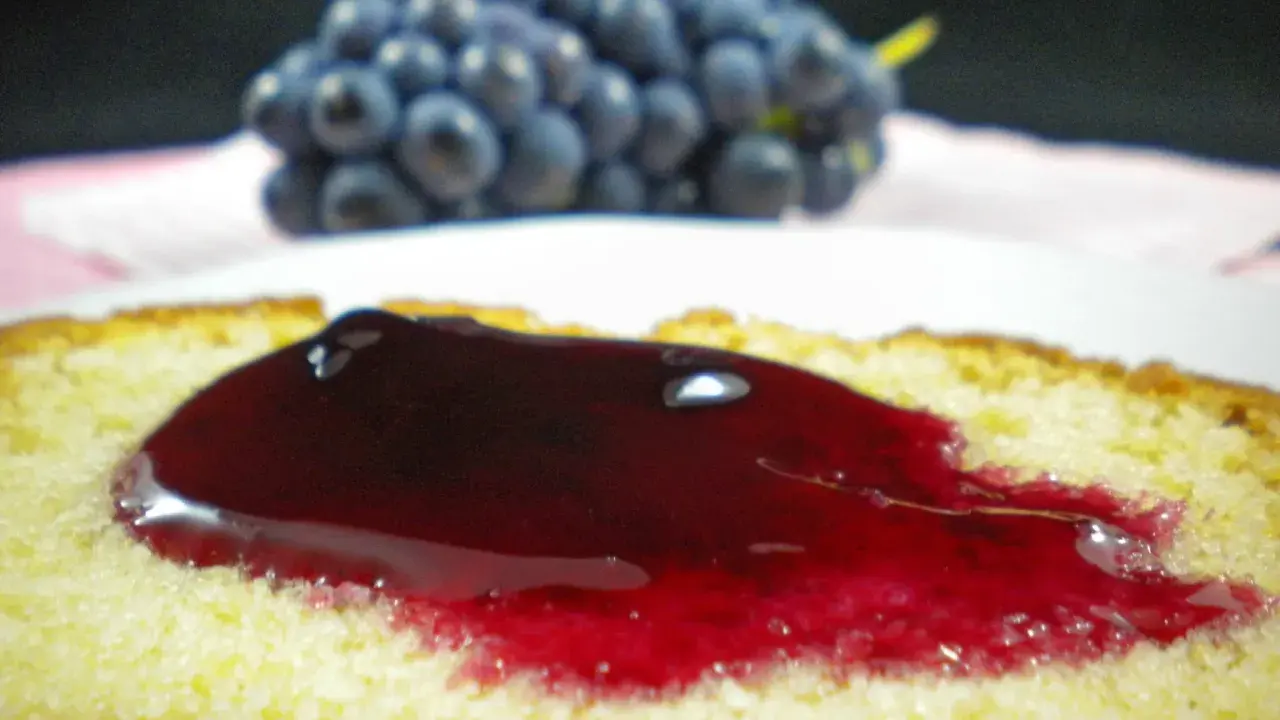 Tranche de gâteau moelleux nappée d'une généreuse gelée de raisin, avec une grappe de raisins bleus en arrière-plan.