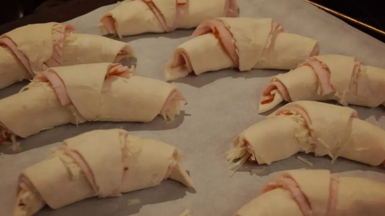 Huit croissants garnis de jambon et de fromage, prêts à être cuits. Une délicieuse pâte à pâte pour un en-cas savoureux.