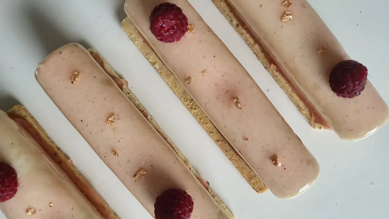 Quatre délicieux rectangles de crème chiboust ou diplomate, ornés de framboises fraîches et de feuilles d'or comestibles.