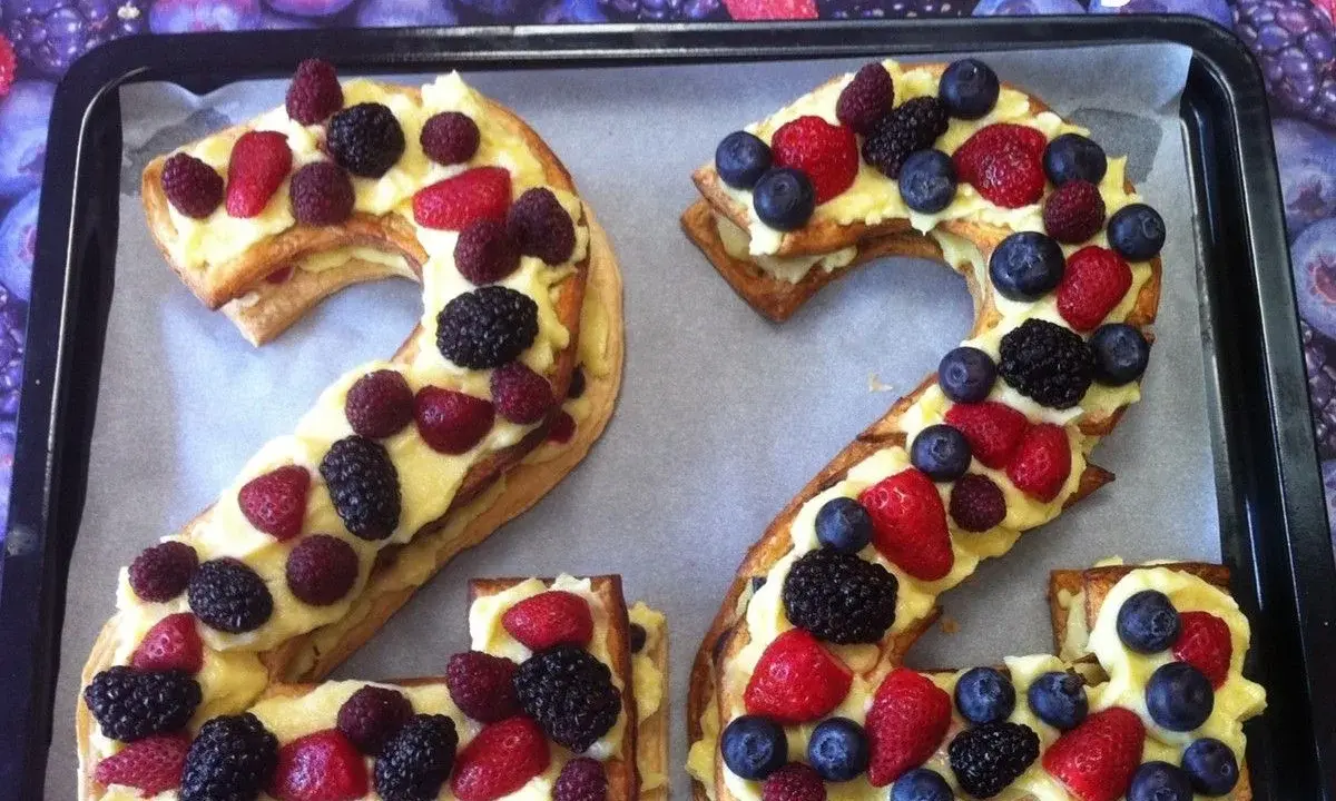 Un délicieux number cake aux fruits rouges, formant les chiffres 2 et 4, garni de crème pâtissière et de baies fraîches.