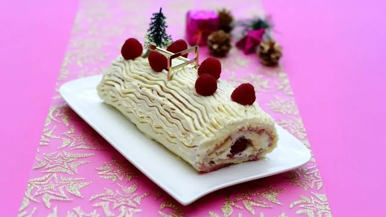 Bûche de Noël au chocolat blanc et framboise, décorée de fruits rouges et d'un petit sapin. Une délicieuse recette pour les fêtes.