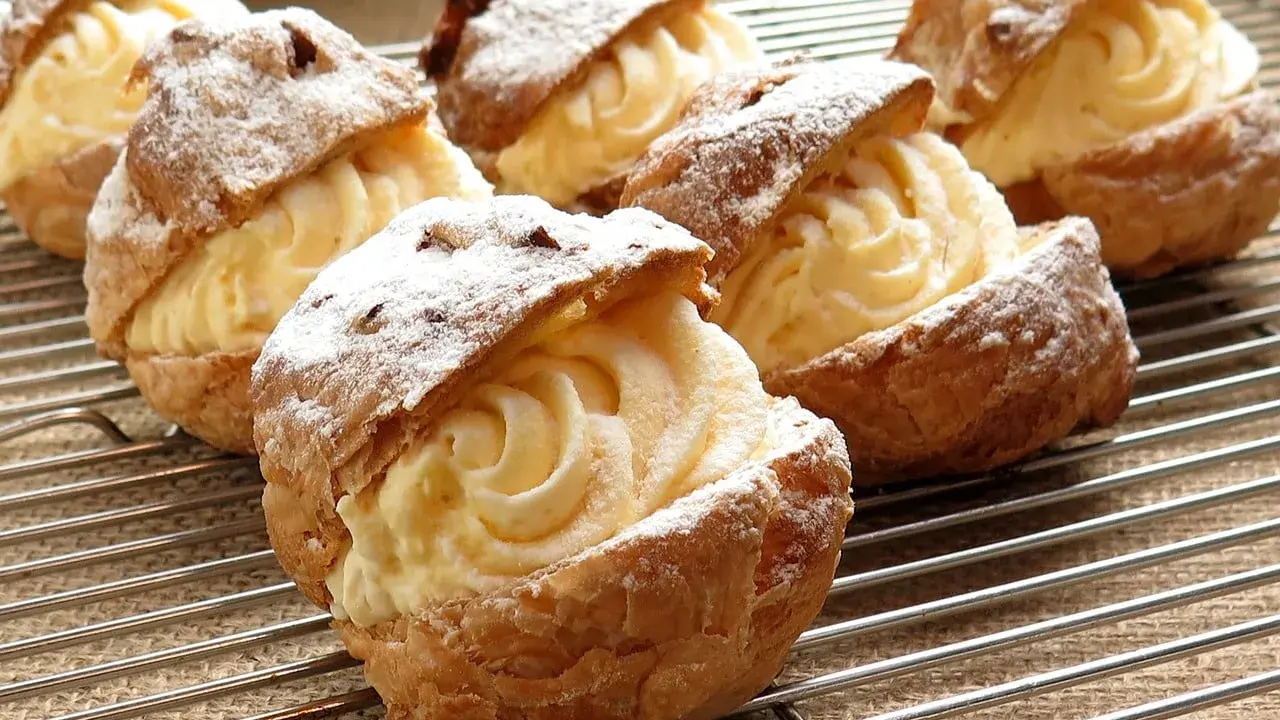 Pâte à choux au robot, garnies d'une crème onctueuse et saupoudrées de sucre glace, refroidissent sur une grille.