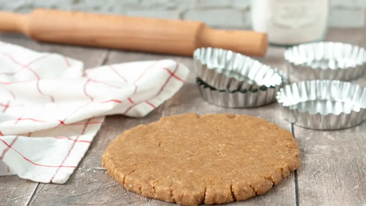 Pâte sablée prête pour la cuisson au four à chaleur tournante. Rouleau à pâtisserie, moules et torchon à proximité.