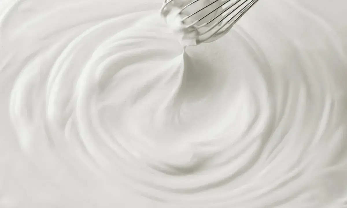 Un fouet mélangeant une crème chantilly aérienne, créant des tourbillons doux et onctueux.