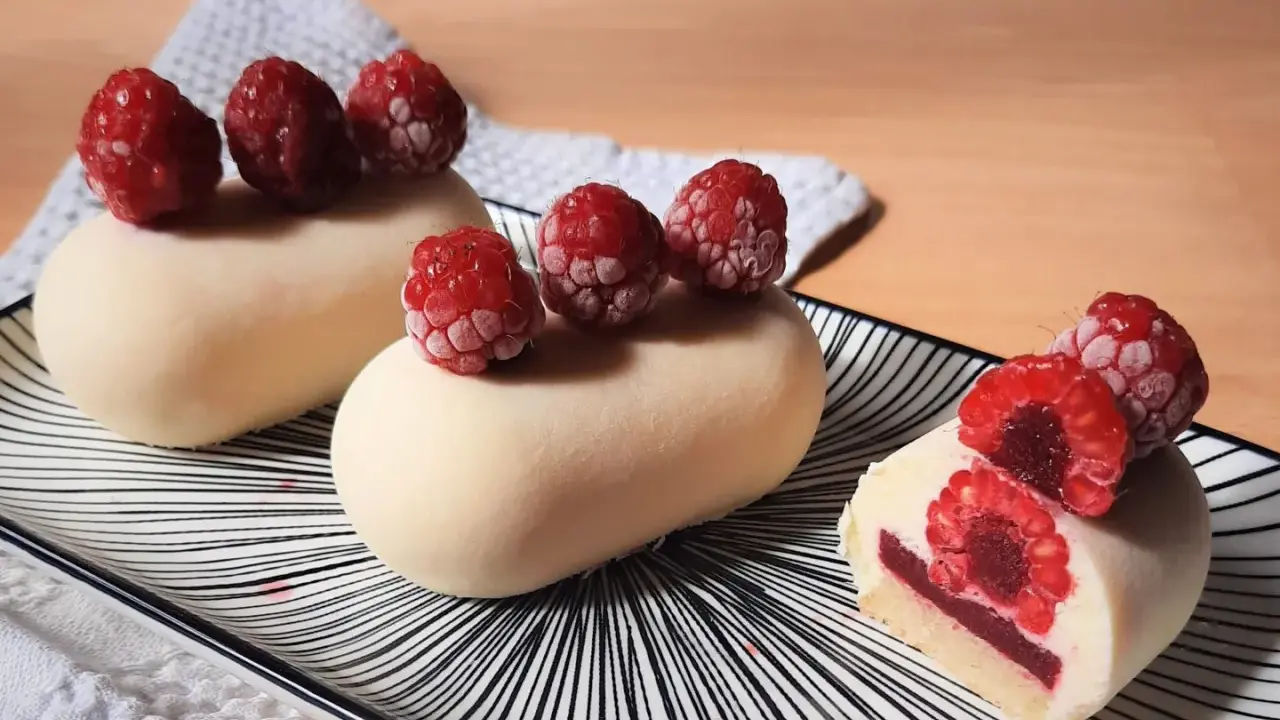 Entremets vanille-framboise sur assiette rayée, décorés de framboises fraîches.