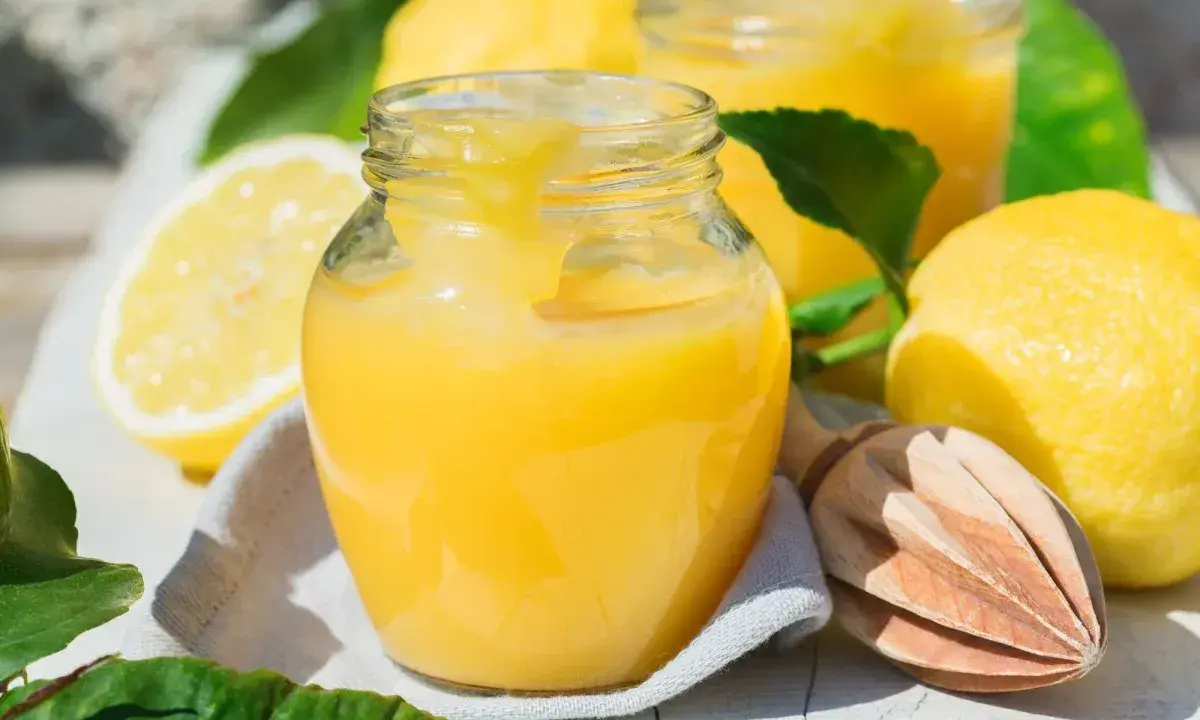 Un pot de crème au citron onctueuse, avec des citrons frais et une presse à bois. Parfait pour une tarte ou une crème dessert.