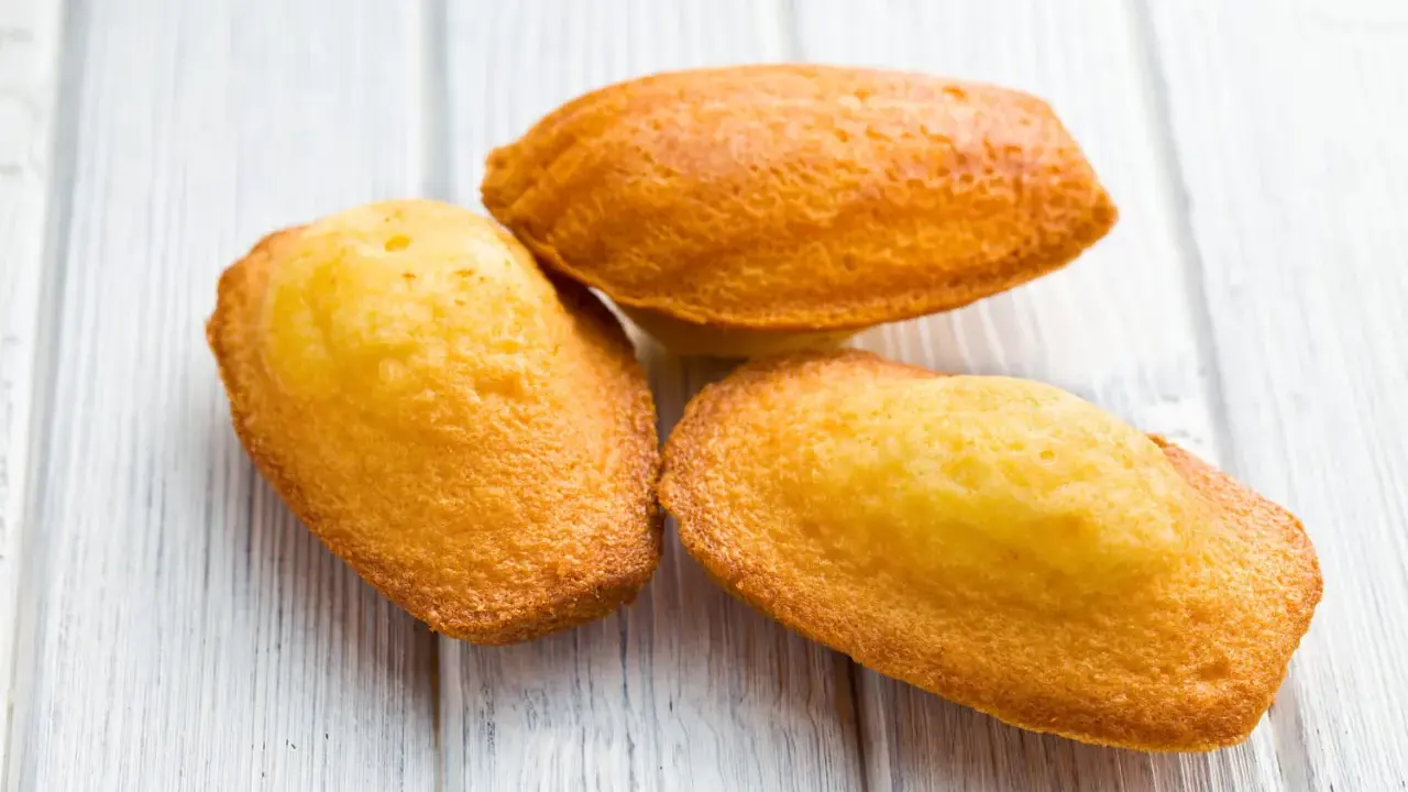 Trois madeleines dorées, parfaites pour la meilleure recette madeleine, sur un fond de bois clair.