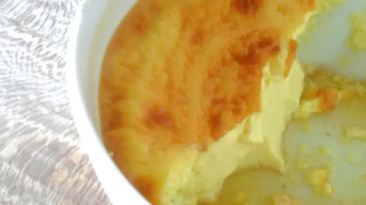 Un flan aux œufs à l'ancienne, doré et crémeux, servi dans un plat blanc sur une nappe texturée.