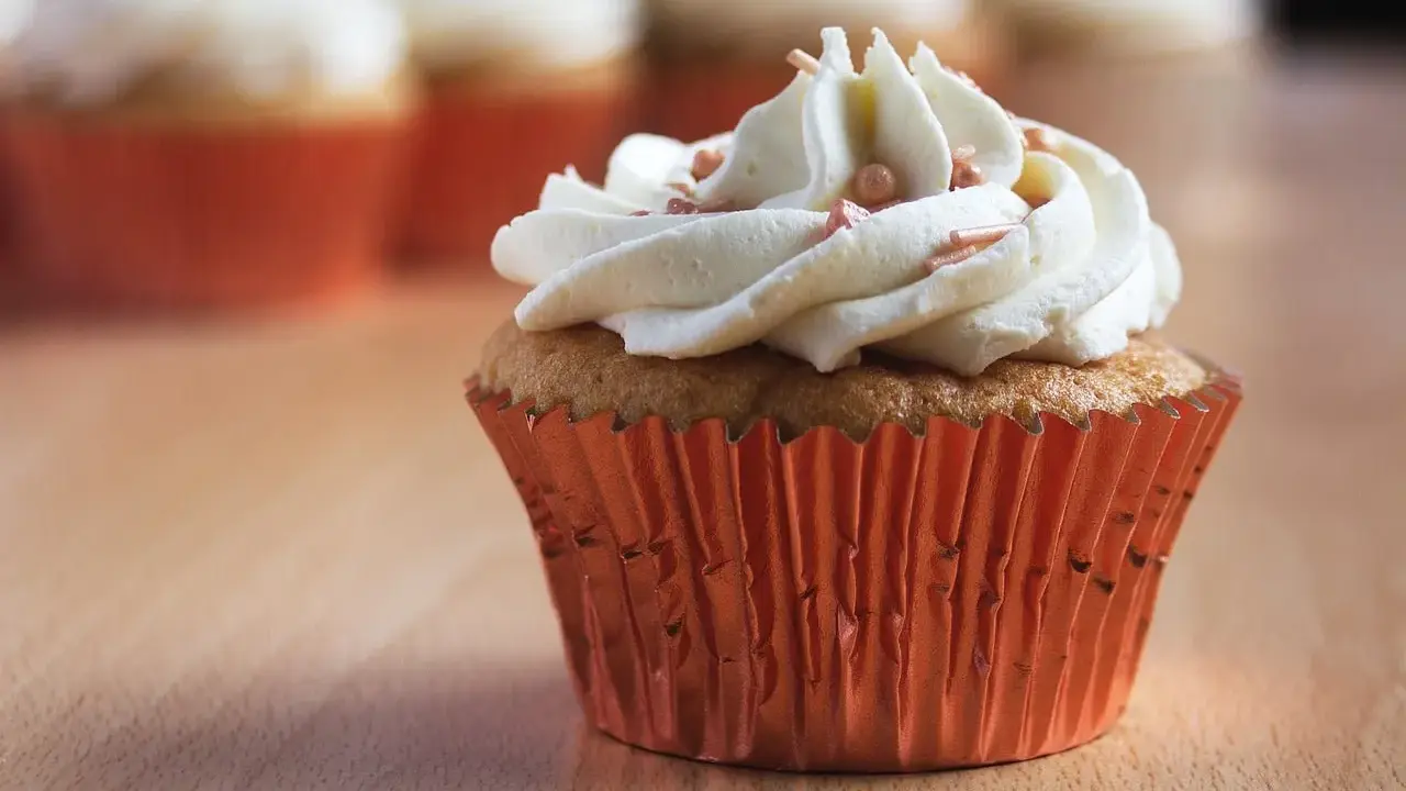 Un cupcake orné d'une généreuse ganache chocolat blanc, parsemé de perles rosées, dans un élégant caissette orange.