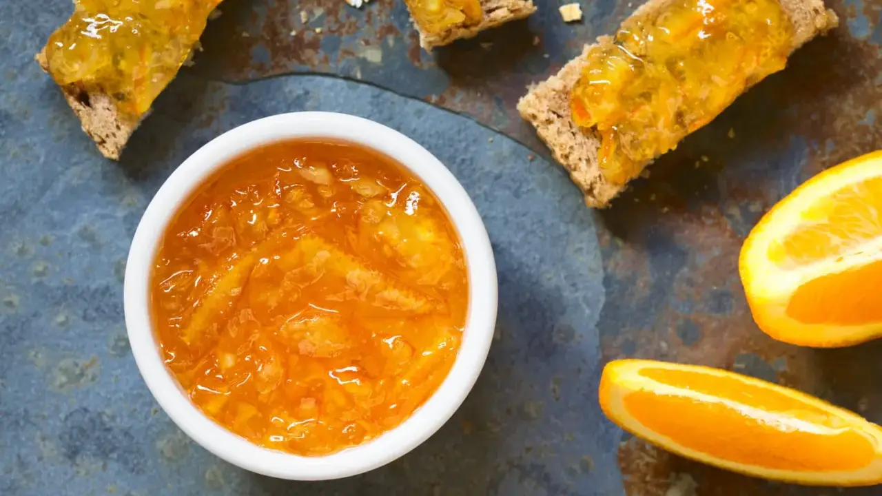 Confiture d'écorce d'orange brillante dans un bol blanc, servie sur des toasts avec des tranches d'orange fraîche.