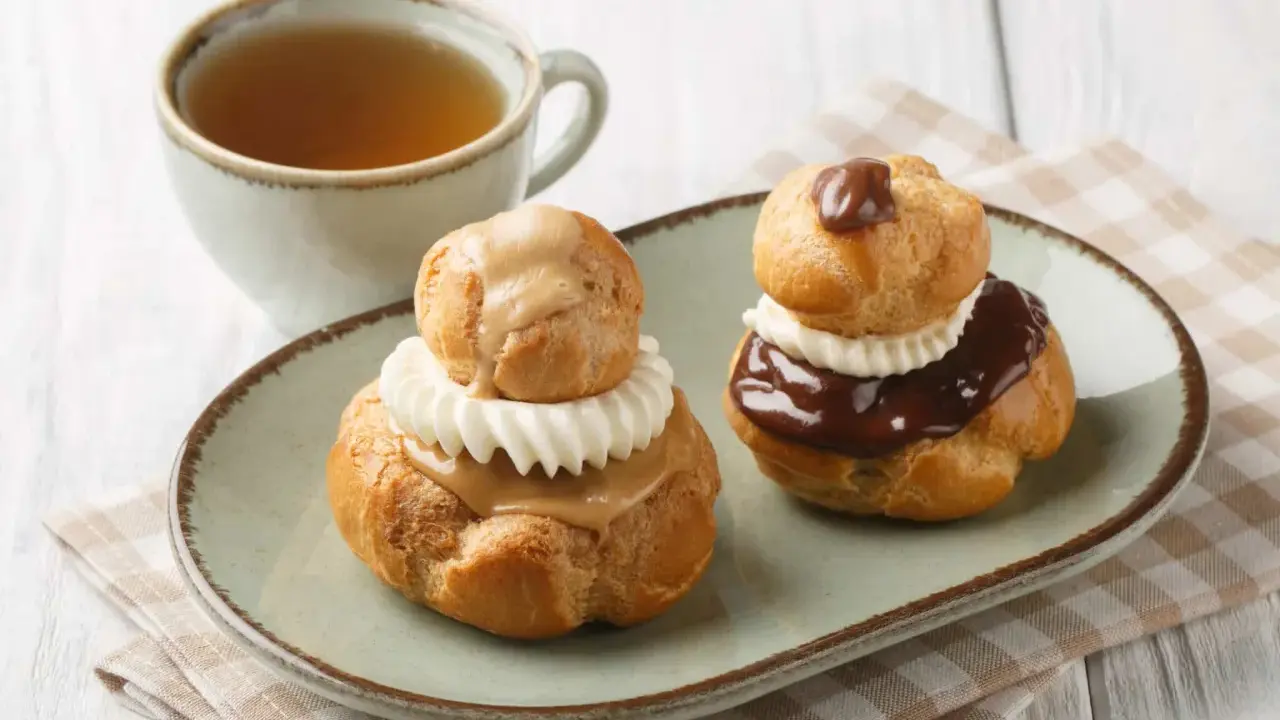 Deux religieuses au café, garnies de crème et nappées de chocolat ou de caramel, accompagnées d'une tasse de thé.