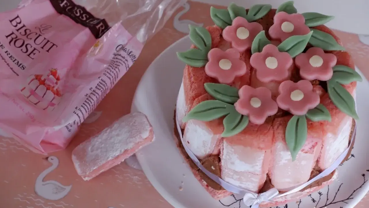 Charlotte aux biscuits roses de Reims, décorée de fleurs en pâte d'amande. Un biscuit rose saupoudré de sucre est à côté.