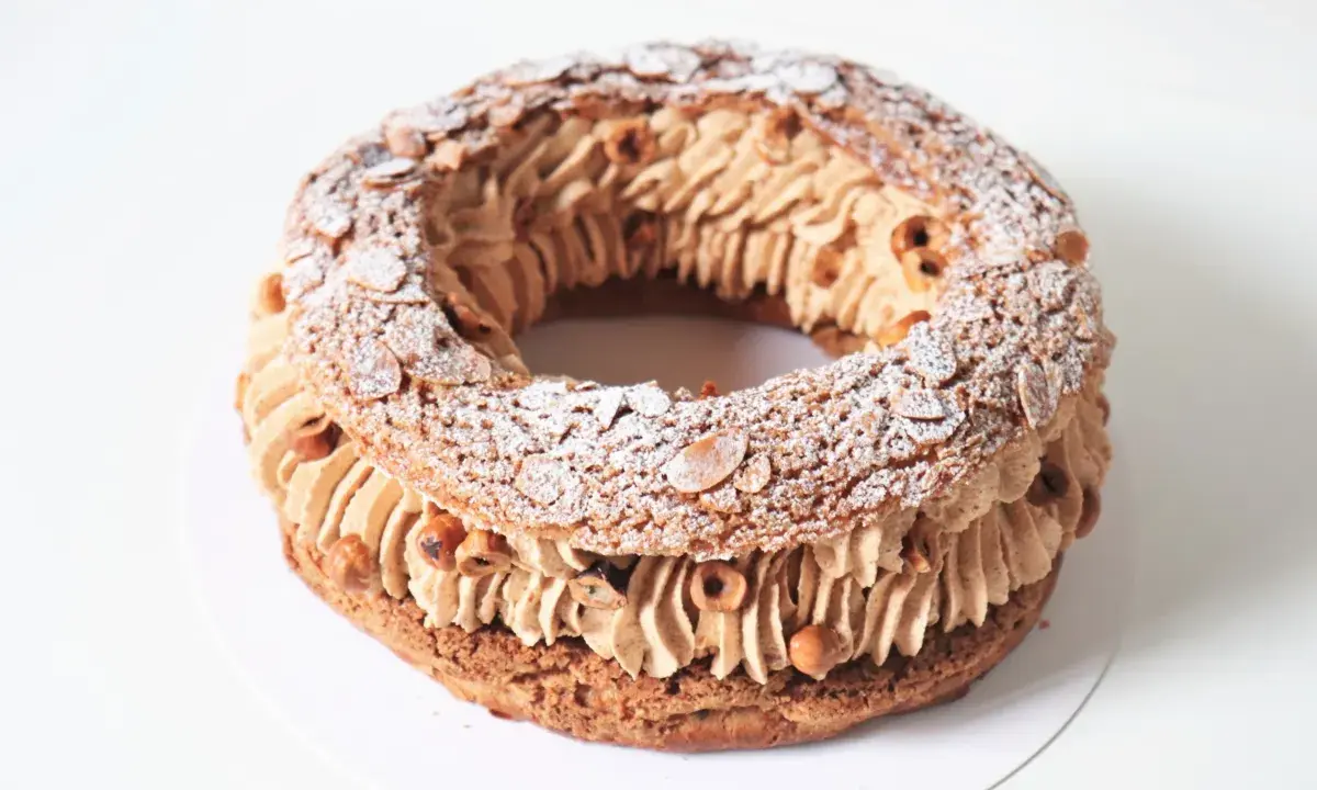 Un Paris Brest meilleur du chef, généreusement garni de crème pralinée et parsemé d'amandes effilées et de noisettes.