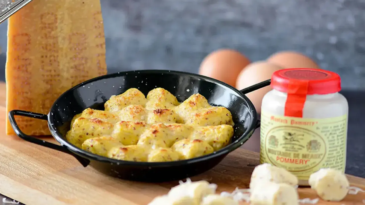 Gnocchi à la parisienne gratinés, servis dans une poêle avec du fromage râpé, des œufs et de la moutarde de Meaux.