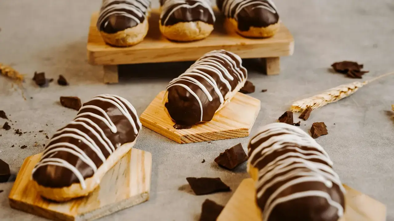 Éclairs gourmands avec un glaçage éclair chocolat brillant, décorés de fines rayures blanches. Des éclats de chocolat parsèment la table.