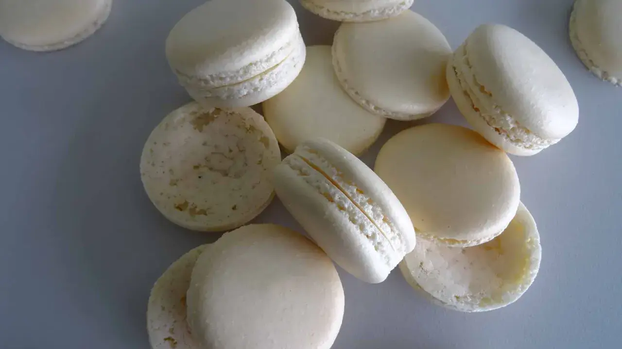 Des macarons blancs, certains assemblés, d'autres séparés, prêts pour la cuisson macaron chaleur tournante.