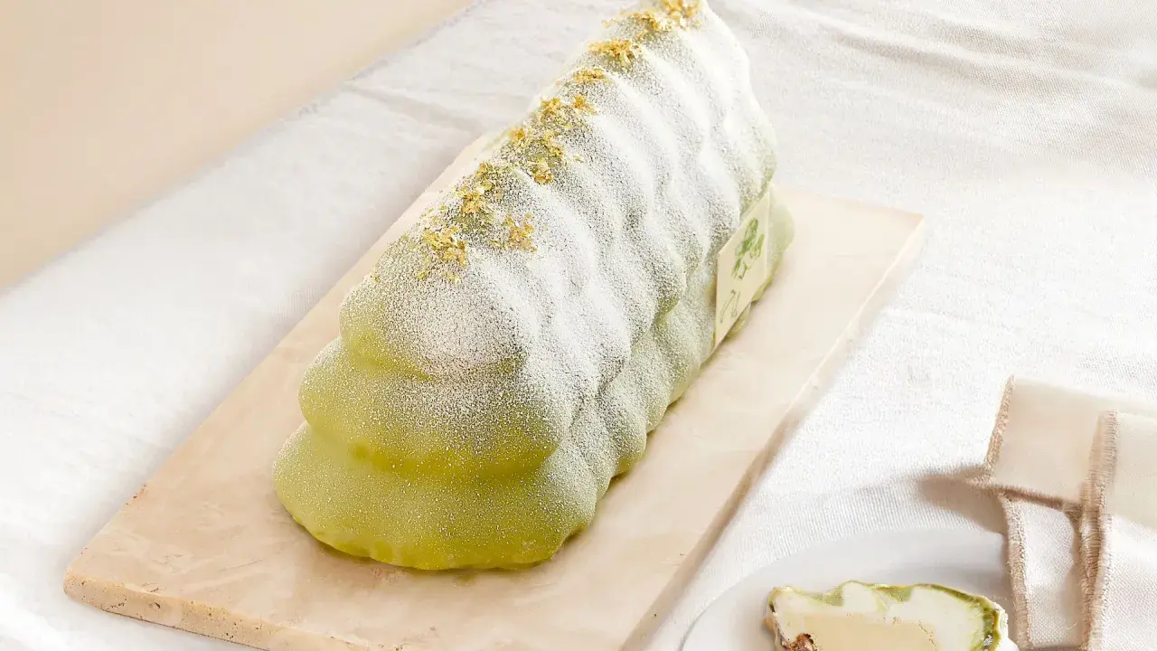 Bûche glacée verte, saupoudrée de sucre glace et de paillettes dorées, évoquant un biscuit madeleine.