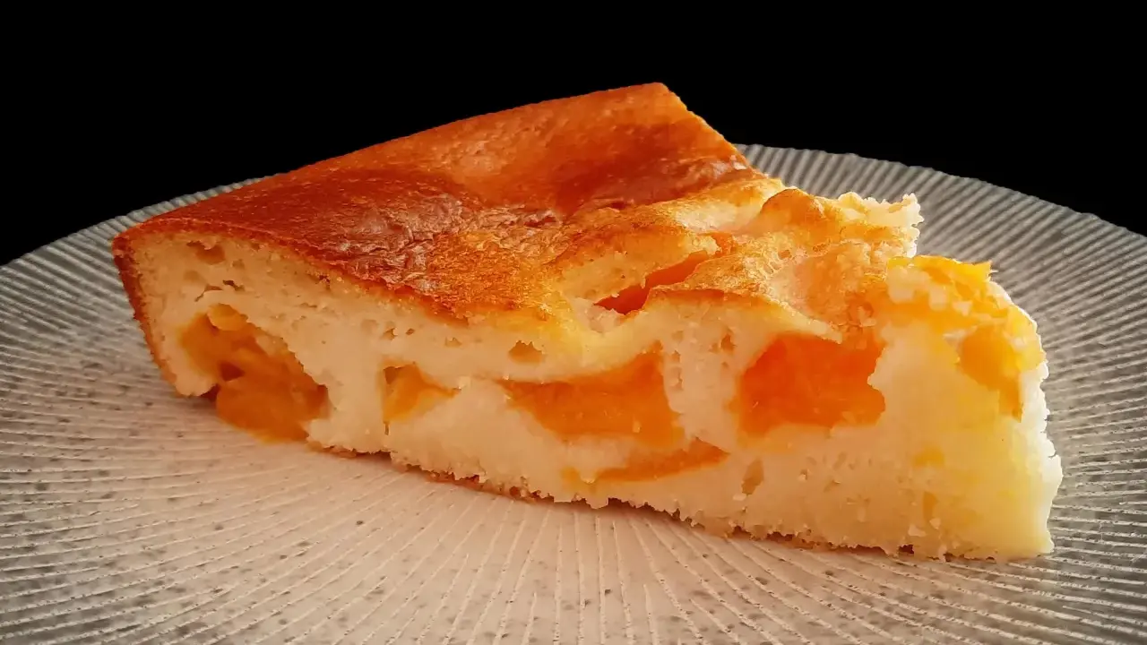 Tranche de clafoutis abricot, une création de chef, sur une assiette texturée.